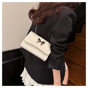 Detail view of a white crinkle leather crossbody bag with a silver butterfly metal buckle