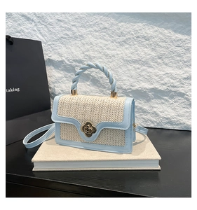 Detail of light blue straw handbag featuring a gold floral lock and spiral handle