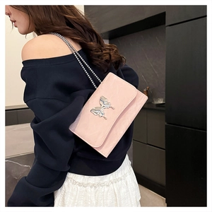 Detail of a pink crossbody bag with a silver butterfly clasp and thin metal chain strap