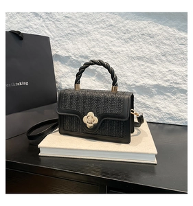 Close-up of black woven leather handbag with gold floral lock and spiral handle detail