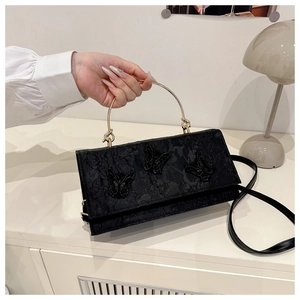 Detail of black crossbody bag featuring butterfly embroidery and gold round handle