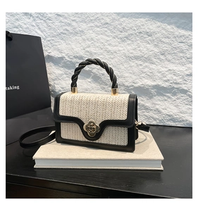 Detail of woven beige handbag with black leather trim and golden flower buckle on a book