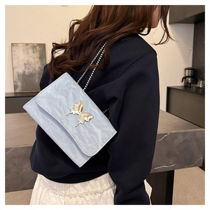 Close-up of light blue pleated bag featuring a large golden butterfly metal buckle