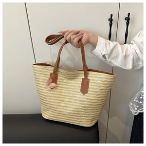 Détail d'un sac cabas en paille tressée avec anses en cuir et décoration de nœud en mousseline