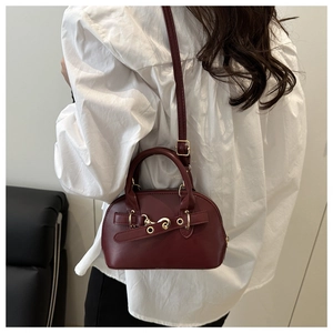 Vista posteriore di una modella con borsa bordeaux a conchiglia, cerniere oro e fibbia retrò