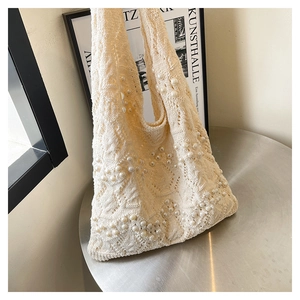 Detail of knit crochet tote bag featuring intricate openwork patterns and faux pearl accents