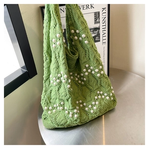 Detail view of green hollow-out knit tote bag featuring decorative white pearls on silver table