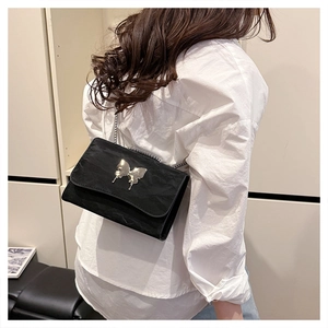 Detail showing a black chain shoulder bag with a silver butterfly buckle on white shirt