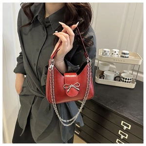 Detail of red crescent shoulder bag featuring silver metal bow and dual chain straps