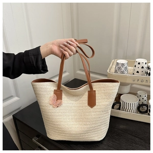 Détail du sac cabas en paille tressée avec anses en cuir marron et charm de ruban rose doux