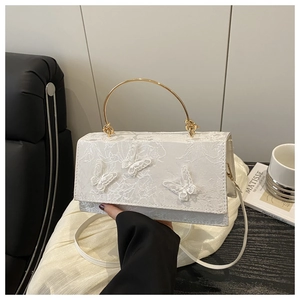 Detail of white lace butterfly bag featuring a gold ring handle and 3D floral accents