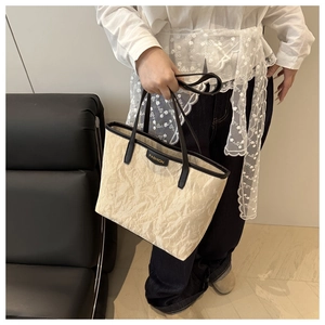 Detail of beige pleated tote bag with black strap and golden FASHION metal logo