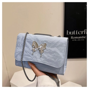 Gros plan sur sac bandoulière bleu clair à texture froissée avec papillon métallique chic
