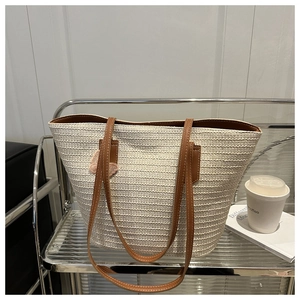 Détail d'un sac cabas en paille tissée avec poignées en cuir marron et patch papillon rose