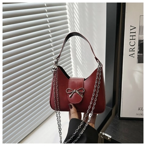 Detail of burgundy mini handbag with silver bow charm and elegant metal chain strap