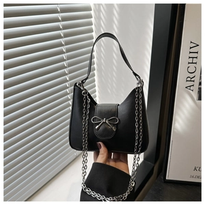 Detail of a black handbag featuring a silver metal bow buckle and elegant chain strap