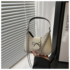 Close-up of cream shoulder bag featuring a silver metal bow and delicate chain strap