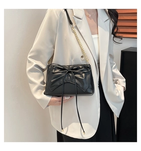 Detail of black matte leather shoulder bag with a large bow and gold chain strap