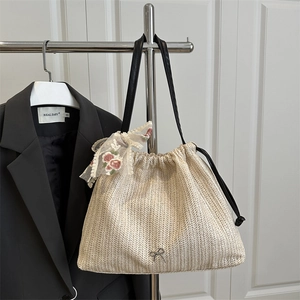 Straw woven tote bag with black leather straps and floral lace bow on white background