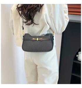 Detail of black textured leather bag with bow and gold metal buckle on female model