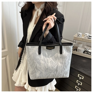 Détail du sac fourre-tout argenté avec texture froissée, anses noires et logo doré