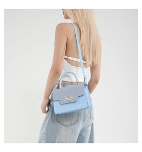 Detail of light blue crossbody bag with dark blue textured flap and gold metal buckle