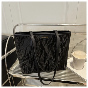 Detail of black glossy crinkled tote bag with golden Fashion logo on a metal shelf