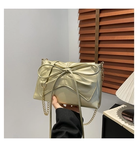Detailed shot of a champagne gold crossbody bag with a large bow and gold chain strap