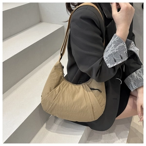 Close-up of khaki nylon crescent bag worn on shoulder by a model in a black blazer