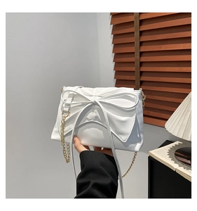 Detail of a white pleated bow handbag with a golden metal chain strap in an elegant setting