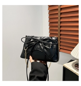 Detail of black crossbody bag featuring a large bow design and gold metal chain strap