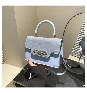 Detail of light blue paneled handbag featuring denim texture and gold buckle