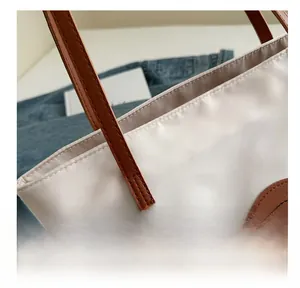 Detailed view of stitch craftsmanship on beige tote bag with brown leather handles