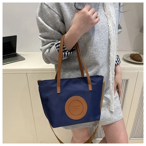 Close-up of a navy nylon tote bag with brown leather handles and FASHION BAGS patch