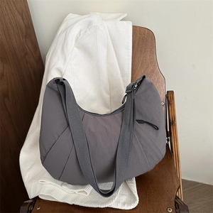 Minimalist grey nylon crescent tote bag with pleated design on a wooden chair