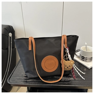 Close-up of black nylon tote bag with leather straps and plush bear charm on a desk