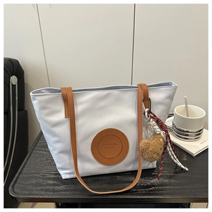 Detail of grey tote bag with brown leather handles and a plush bear pendant on a table