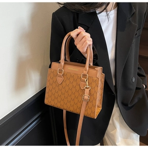 Detail view of brown leather tote bag with M-pattern print and gold hardware