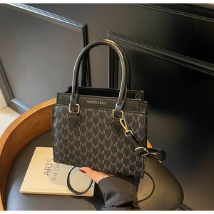 Detail of black faux leather tote with grey M-letter monogram and golden hardware