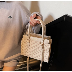 Detail of beige monogram tote bag featuring leather handles and golden hardware accents