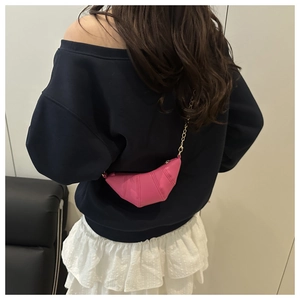 Detailed view of mini croissant bag in vibrant rose pink with gold chain strap worn by model