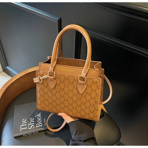 Detail of monogram leather tote bag with gold logo and adjustable strap on a chair