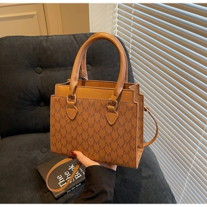 Detail of a brown tote bag with M-pattern texture and detachable thin shoulder strap