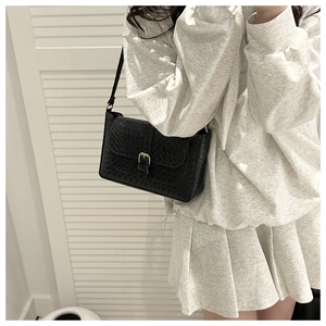 Close-up of black shoulder bag featuring woven texture and metallic buckle on model