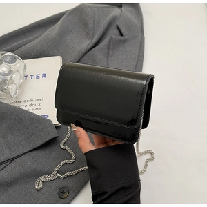 Detail of black glossy chain bag with subtle textured finish on a grey suit jacket