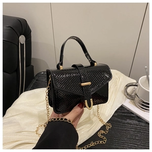 Detail of black snake pattern mini handbag with gold chain strap on white silk background