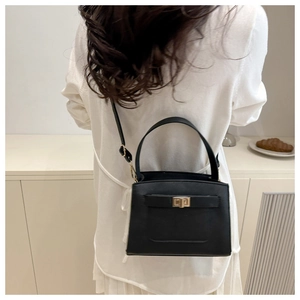 Detail view of the black leather handbag featuring metal lock and adjustable shoulder strap