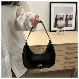 Detail of a black half-moon shoulder bag featuring a delicate silver metal bow accent