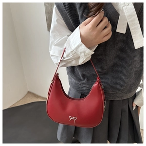 Detail of red crescent leather bag featuring a silver metal bow accent and zipper closure