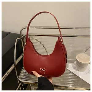 Detail of red crescent leather bag with silver bow buckle held by a model